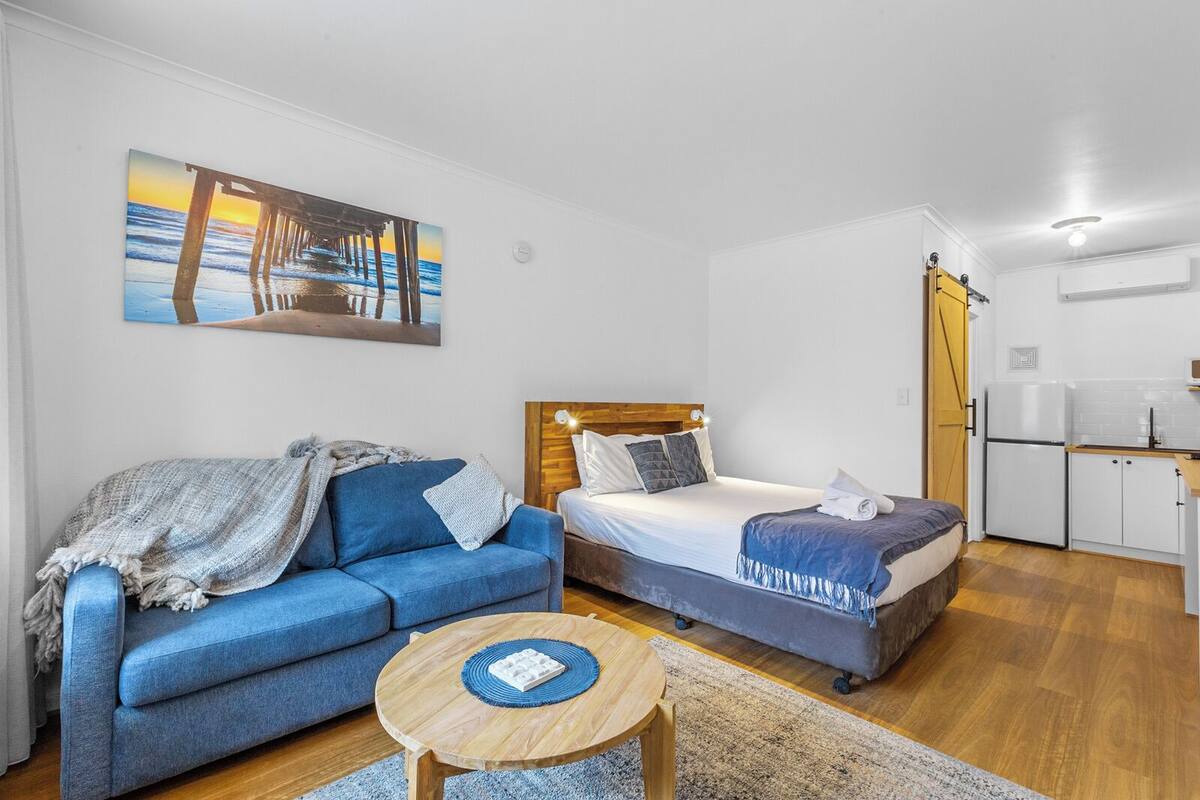 Ett litet rum med en säng, en soffa, ett litet bord och ett litet kök.