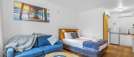 A compact room with a bed, a sofa, a small table, and a kitchenette.