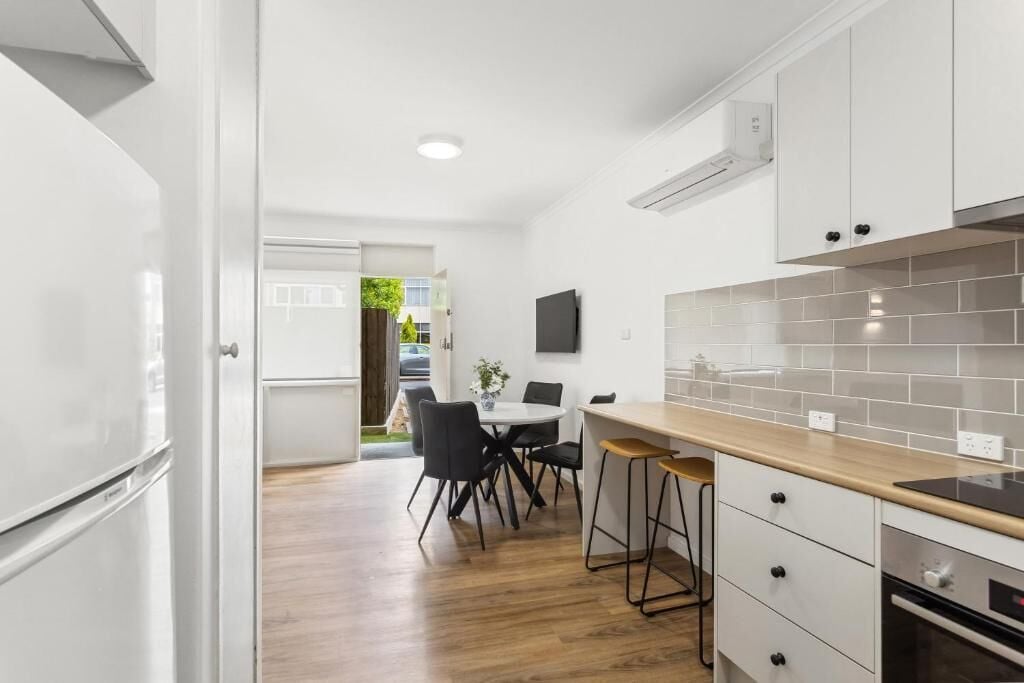A modern kitchen with white cabinetry, a wooden countertop, and a dining area with a table and chairs.