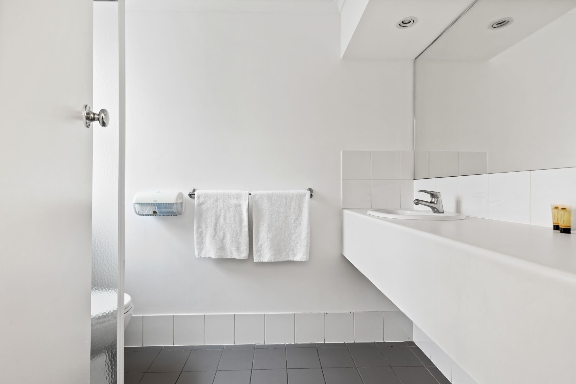 A modern bathroom with a white sink, mirror, and towel rack.