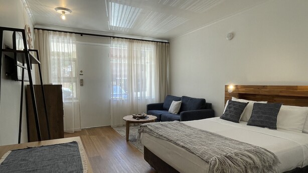 A hotel room with a large bed, a sofa, a small table, and a mirror. - Taft Motor Inn (Glenelg)