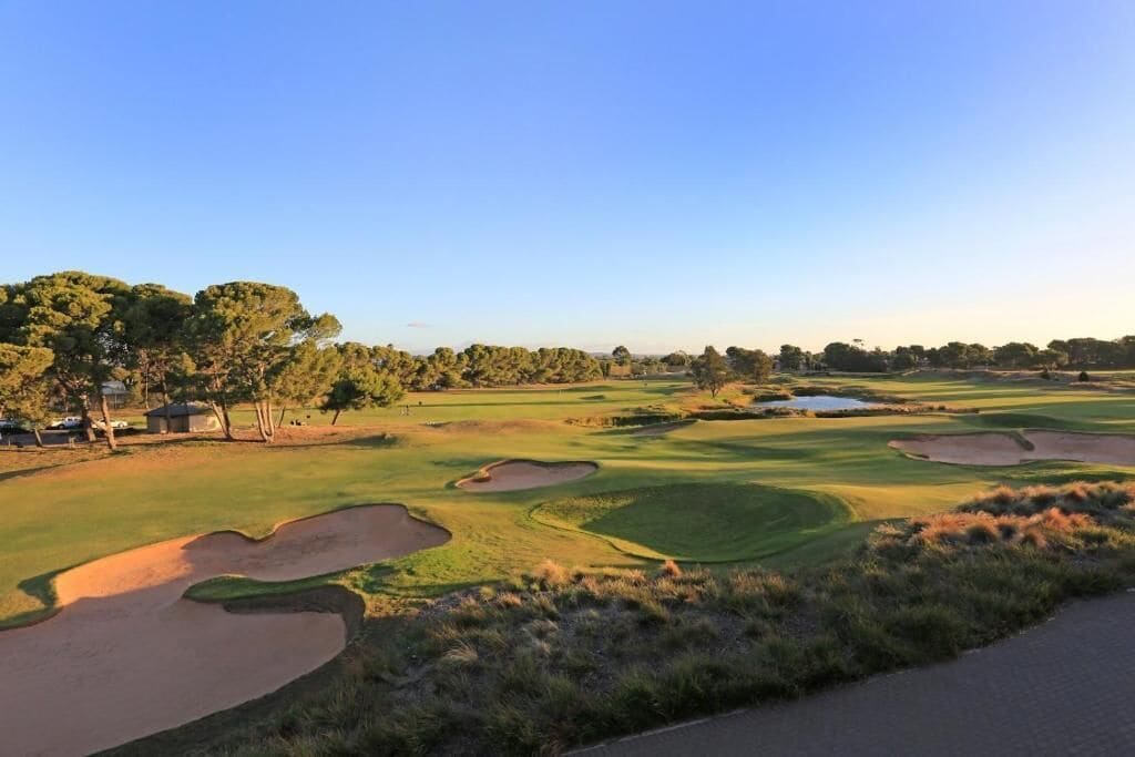 A golf course with sand bunkers, trees, and a clear sky.