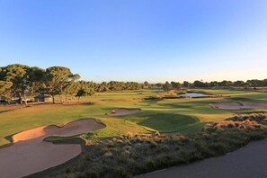 A golf course with sand bunkers, trees, and a clear sky.