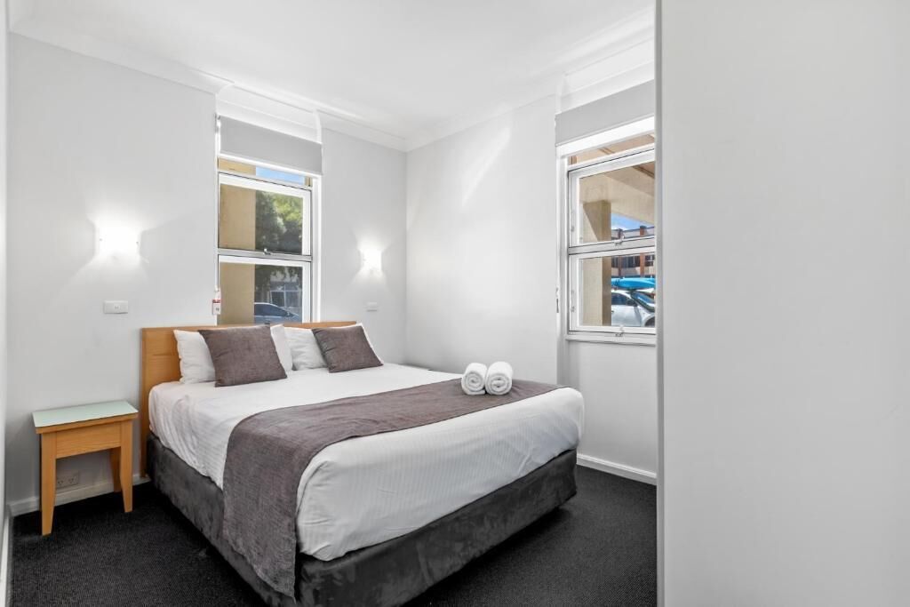 Una habitación de hotel con cama, mesitas de noche y ventanas.