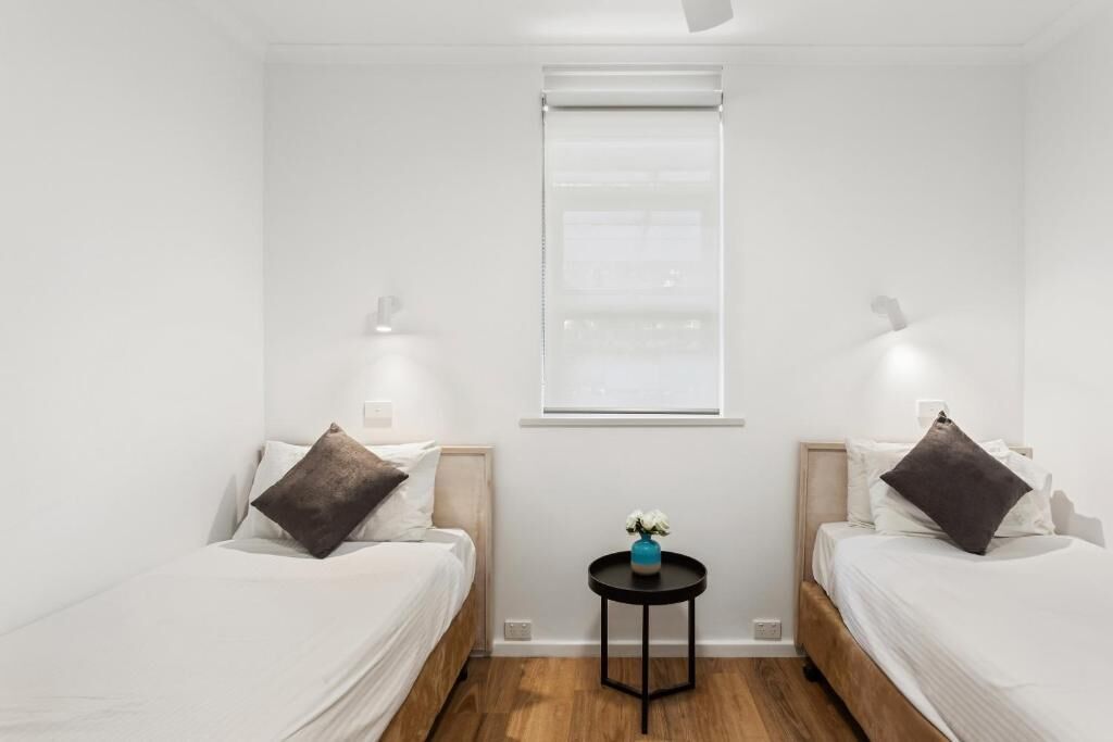 Una habitación de hotel con dos camas, una mesita redonda y una ventana con persianas.