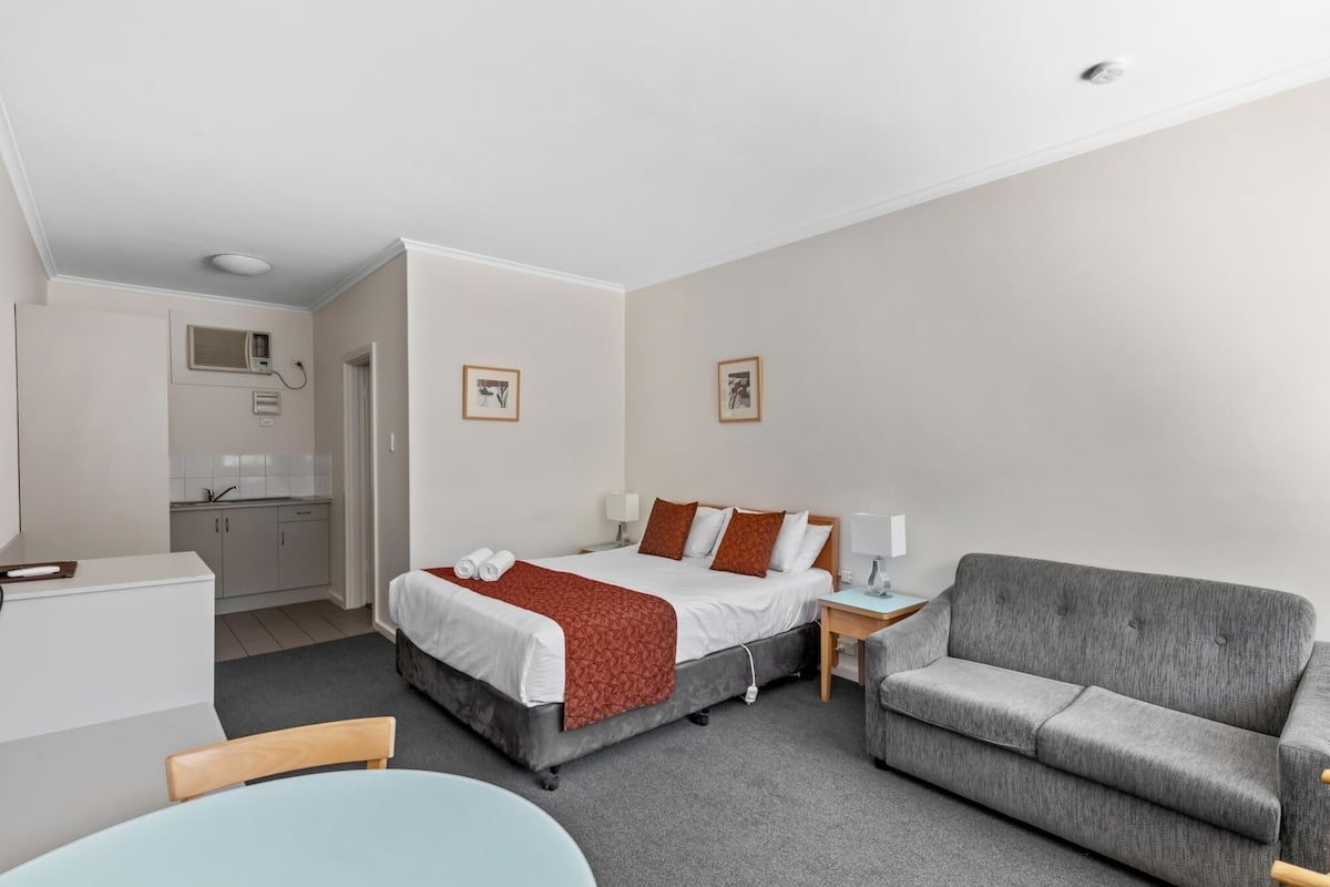 Ett hotellrum med en säng, en grå soffa, ett skrivbord och en stol.