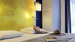 Quarto de hotel com cama, almofadas, chapéu e revista.