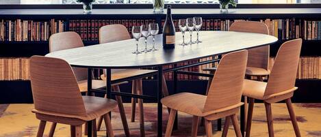 A round table with six wooden chairs, a vase with flowers, and wine glasses on a shelf with books.