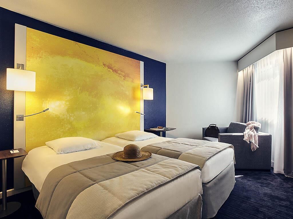 A hotel room with two beds, a large abstract painting on the wall, a desk with a lamp, and a chair.