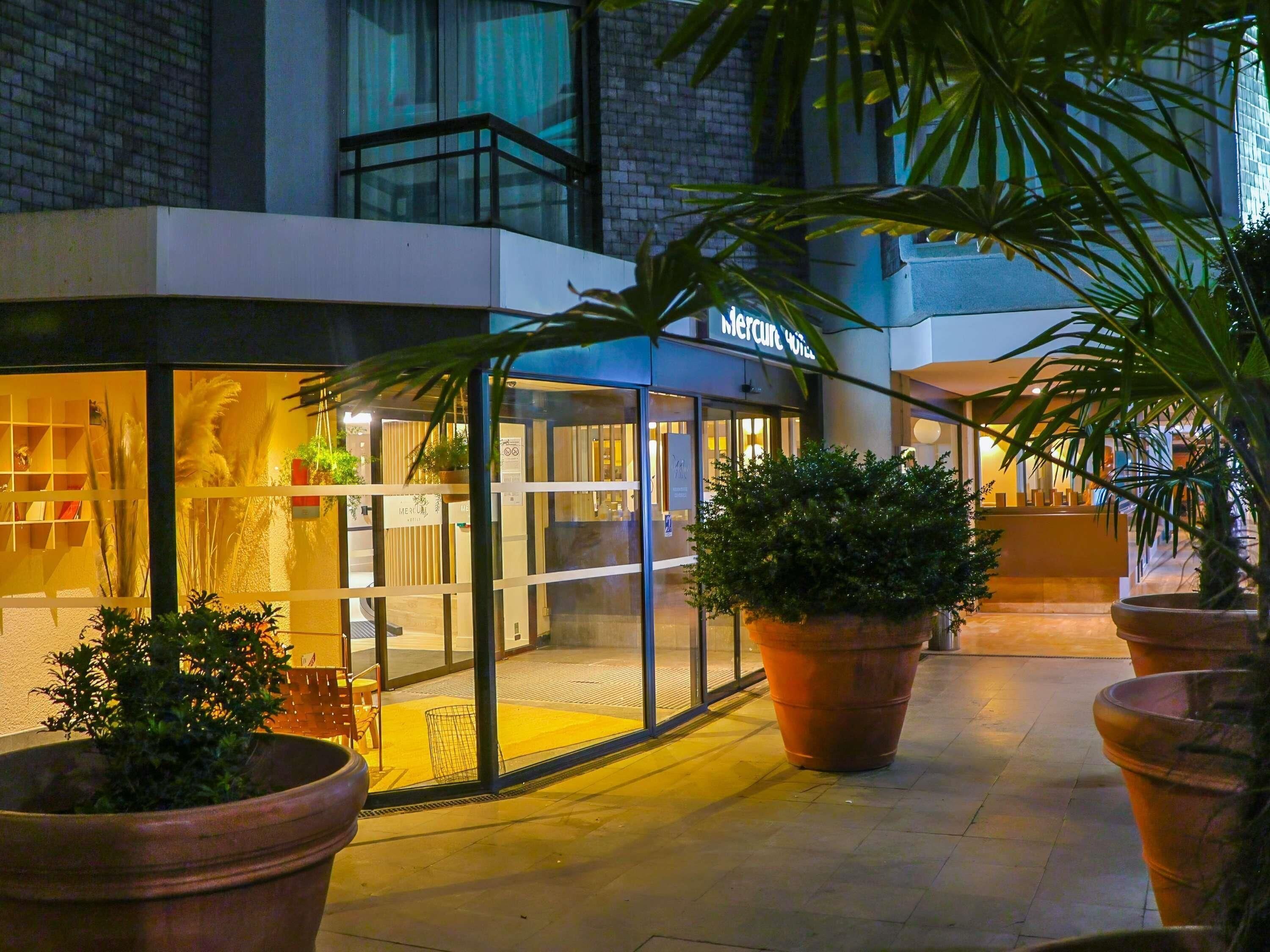 A hotel entrance with a glass facade, large potted plants, and a sign reading "Mercure Hotel".
