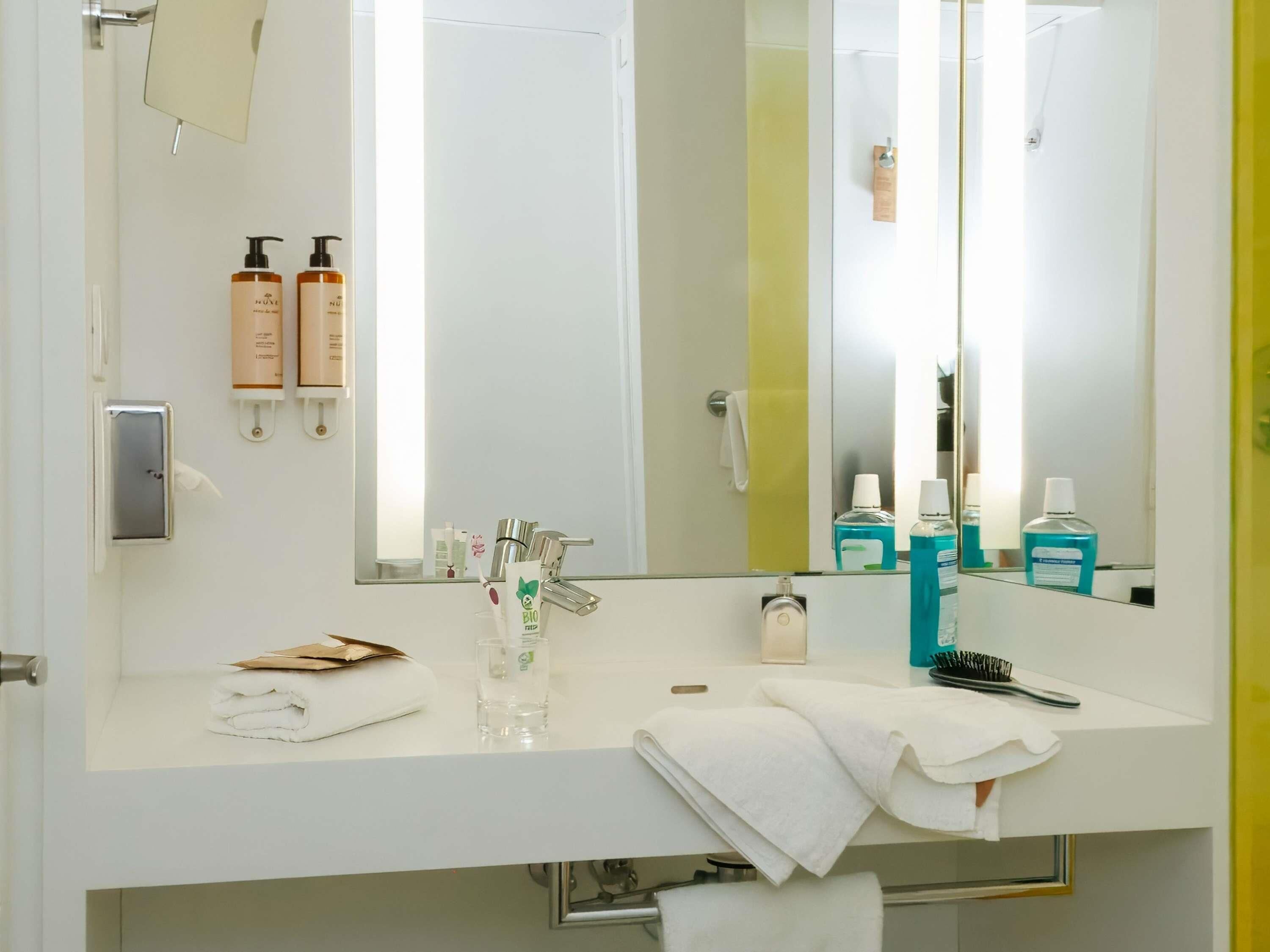 A modern bathroom with a white sink, a large mirror, and toiletries.
