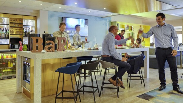 Zona de bar moderna con taburetes, una barra con utensilios y una pantalla de televisión visible.
