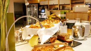 Buffet com diversos produtos de panificação, incluindo doces e pão, e um espaço para café.
