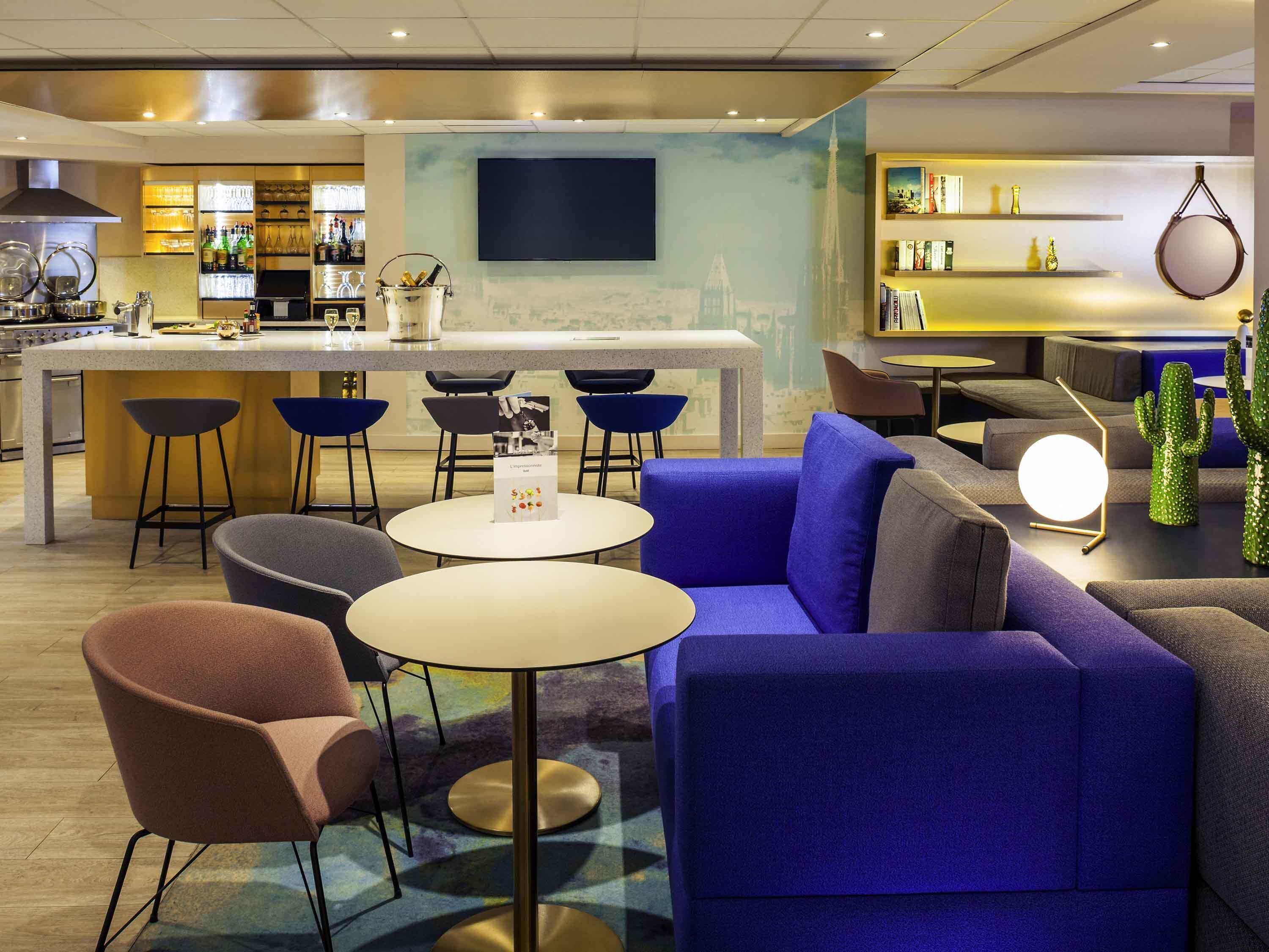 A modern hotel lobby with a bar area, seating arrangements, and a flat-screen TV mounted on the wall.