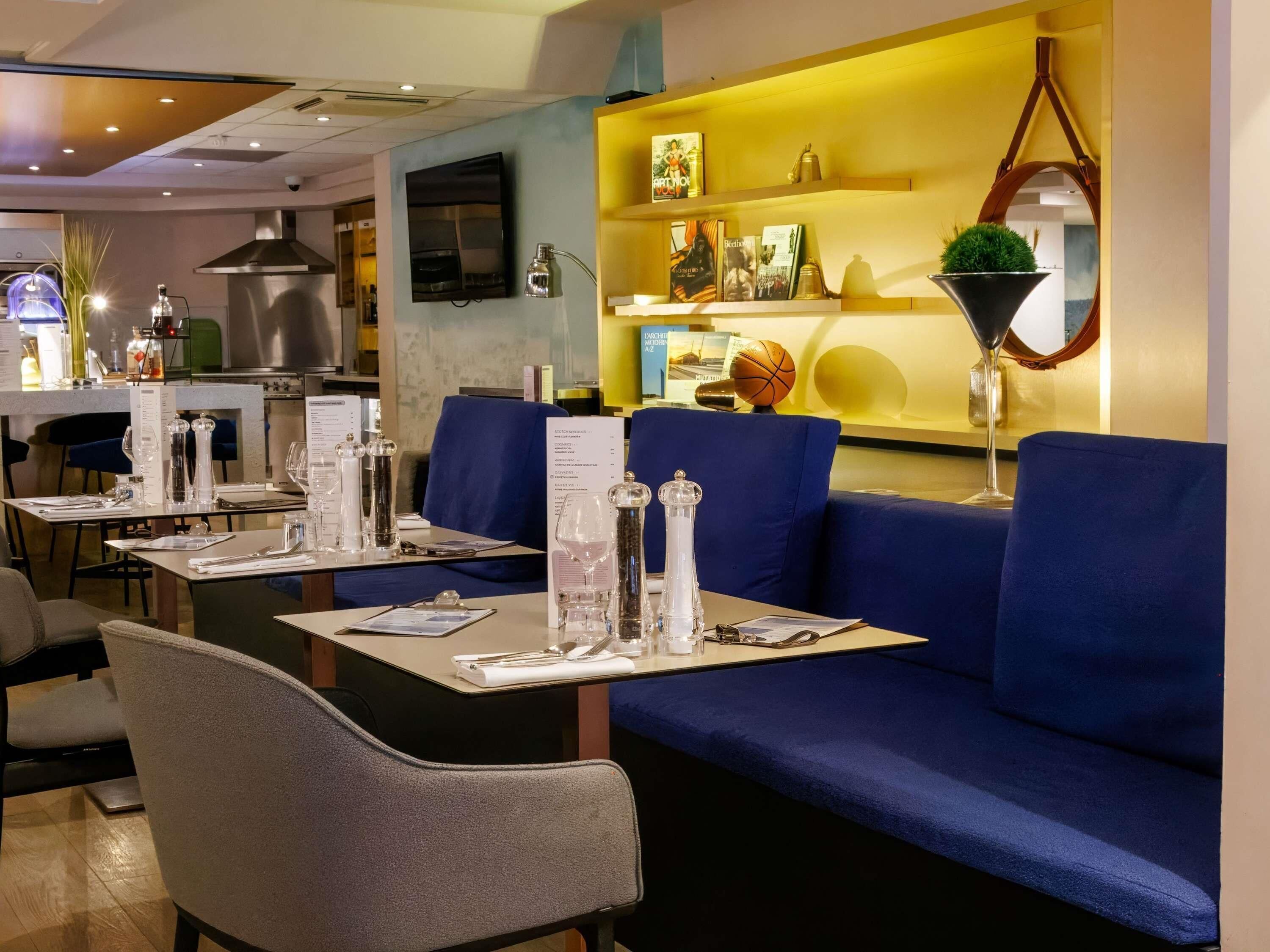 L’intérieur d’un restaurant, avec des sièges bleus, une cuisine en arrière-plan et un présentoir à menus.