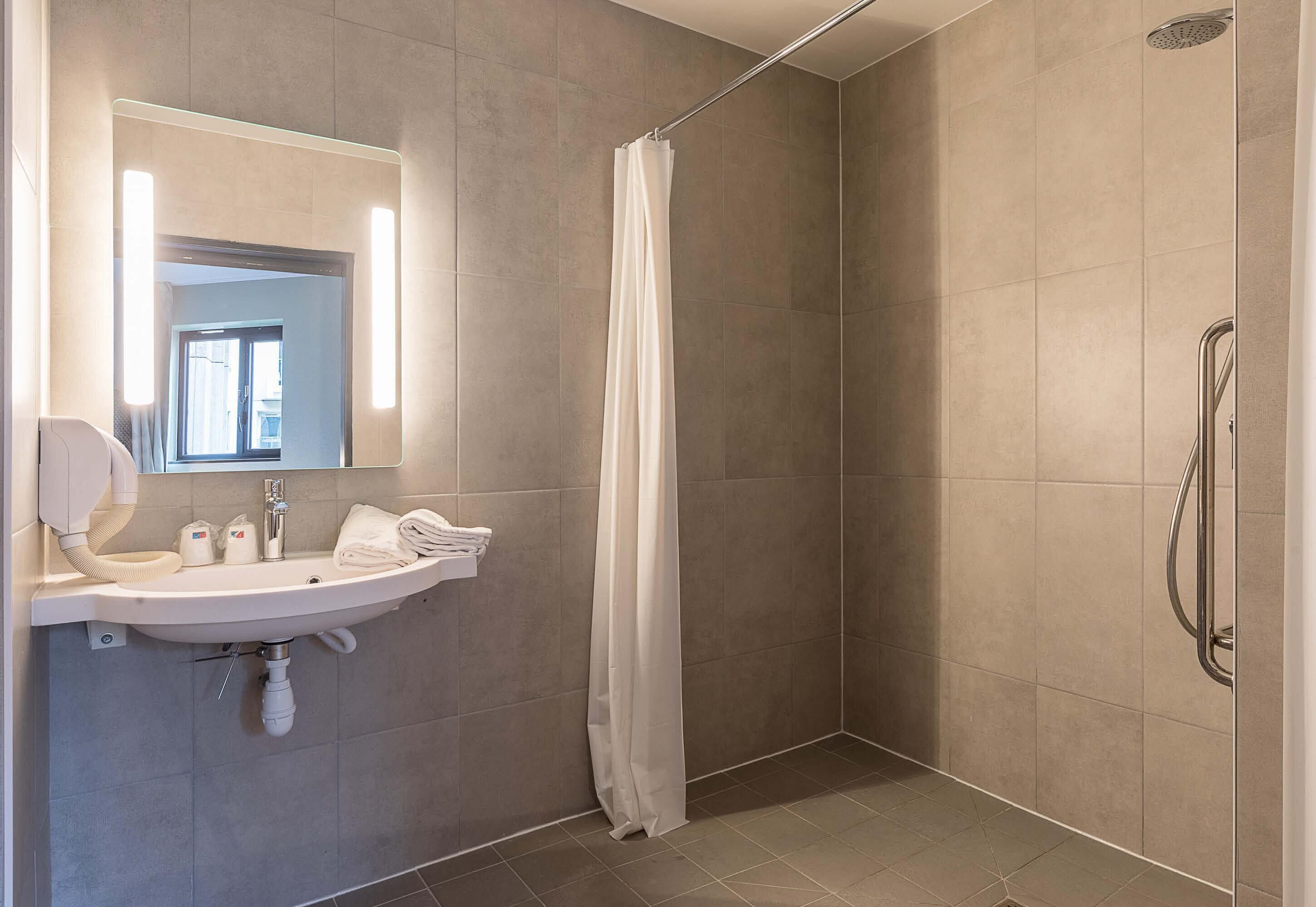 A modern bathroom with a sink, mirror, shower, and a towel rack.