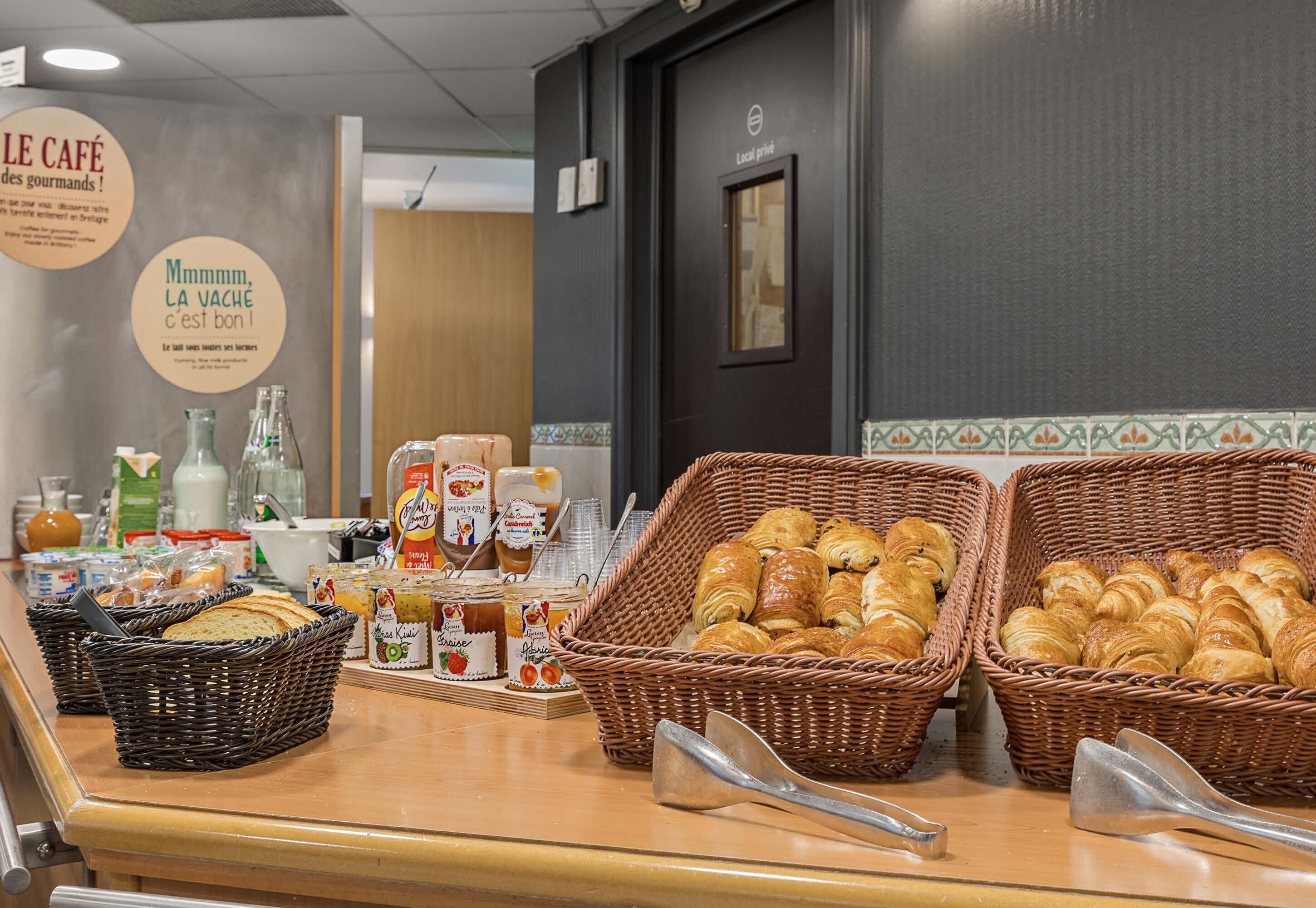 A breakfast buffet with baskets of croissants and other pastries, condiments, and breakfast items.