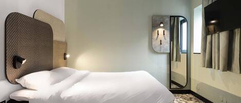 A hotel room with a bed, a wall-mounted light, a mirror, and a large window with curtains.