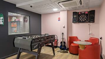 Una habitación con mesa de fútbol, dardo, guitarra y sillas rojas.