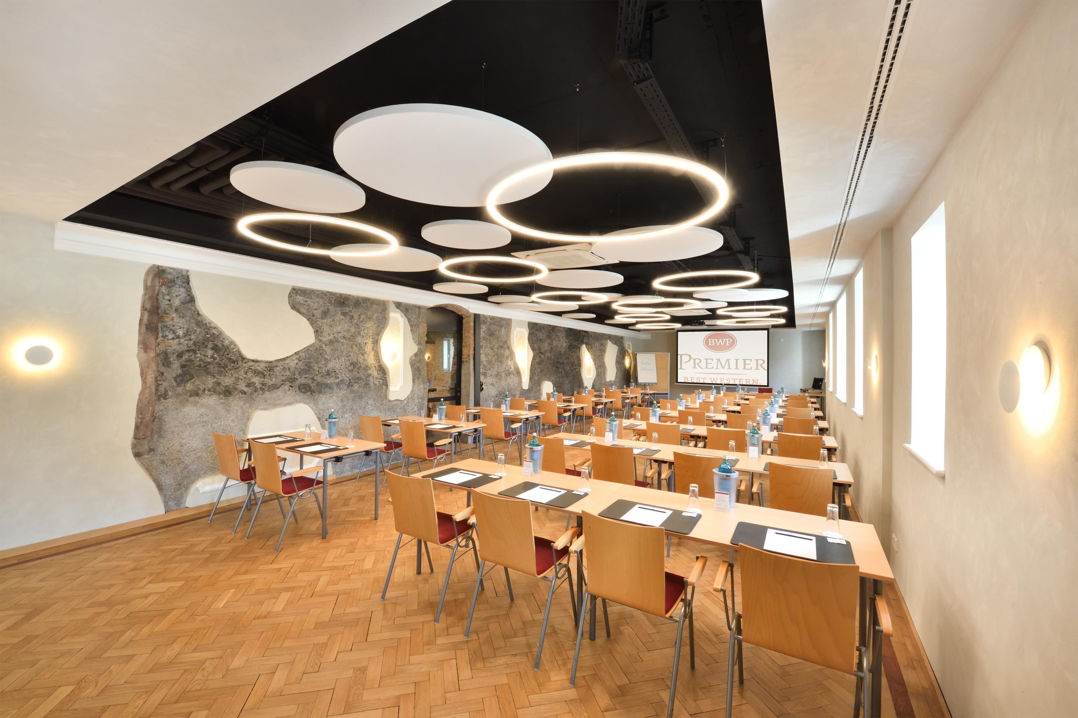 A conference room with multiple tables and chairs, a modern ceiling design with circular light fixtures, and a stone wall feature.