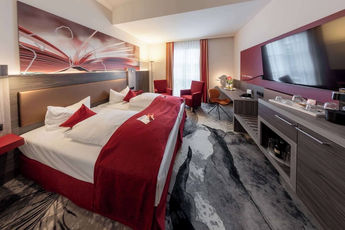 Habitación de hotel con una cama grande, un escritorio, un televisor y un cuadro abstracto moderno en la pared.