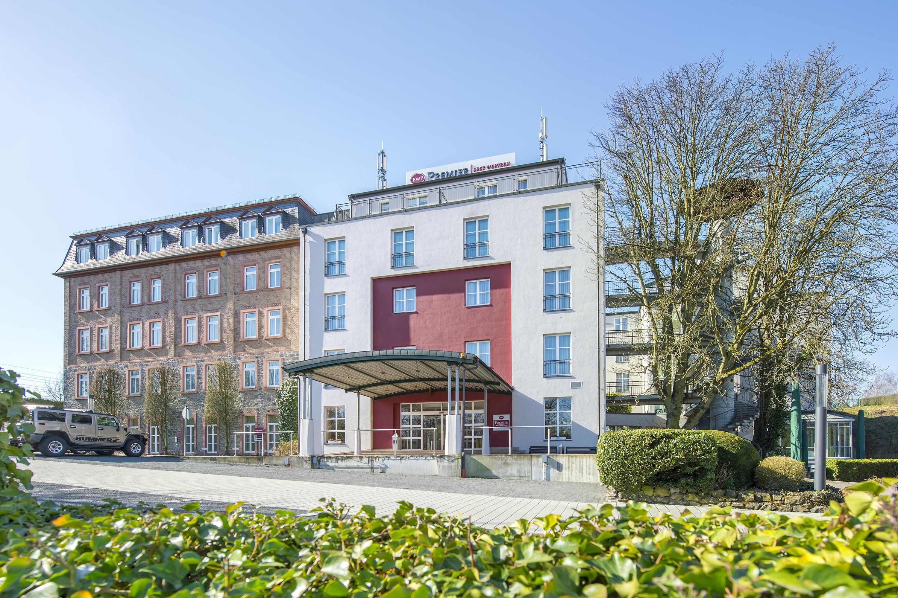 Ein mehrstöckiges Hotel mit roter und weißer Fassade, einem überdachten Eingang und einem Parkplatz mit einem Hummer SUV.