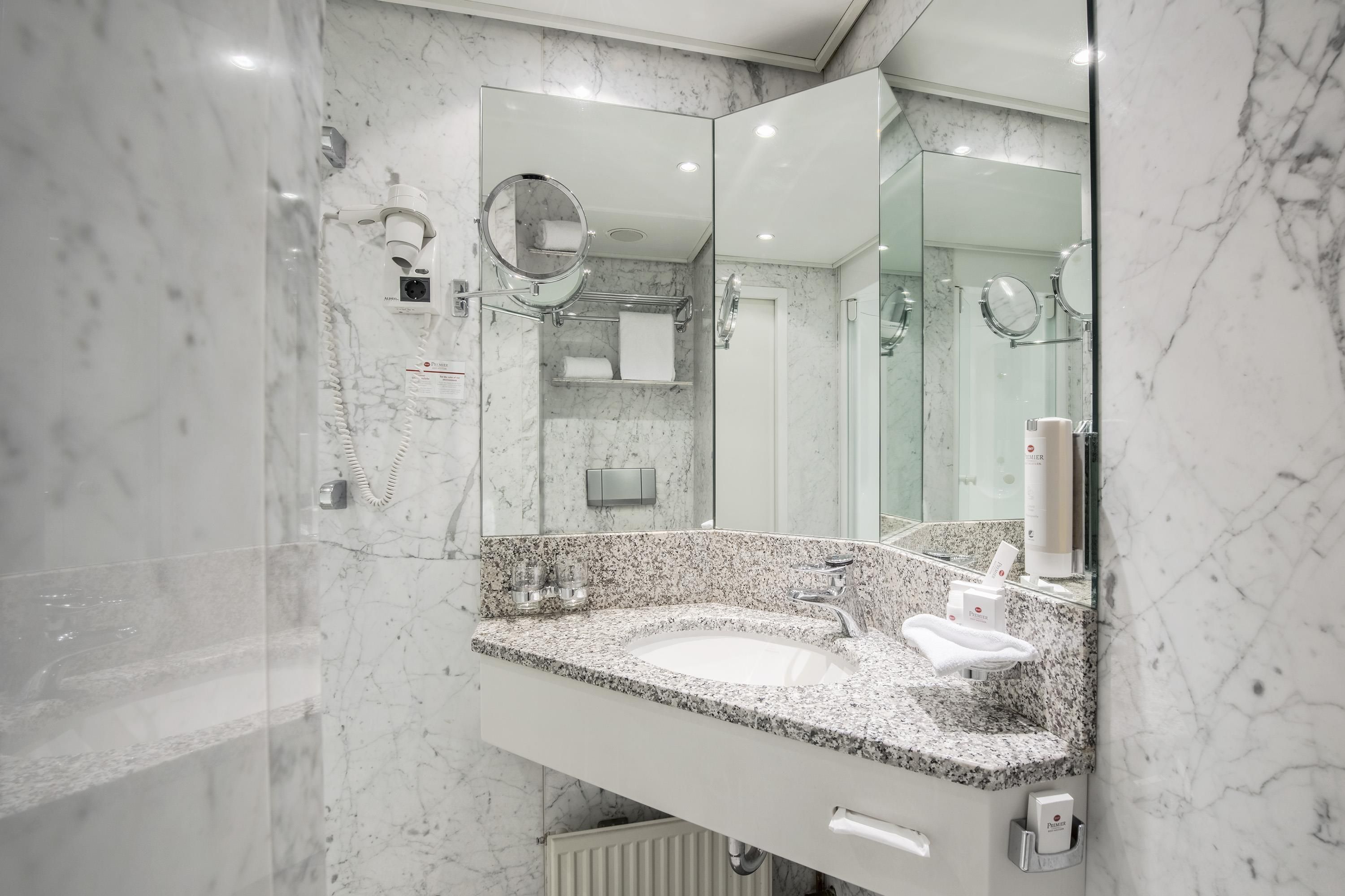 Un baño moderno con tocador de mármol, lavamanos, espejo y cabina de ducha.