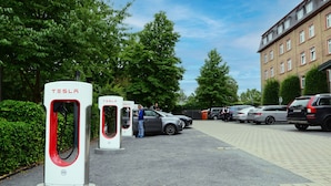 A parking area with electric vehicle charging stations, a building, and parked cars.