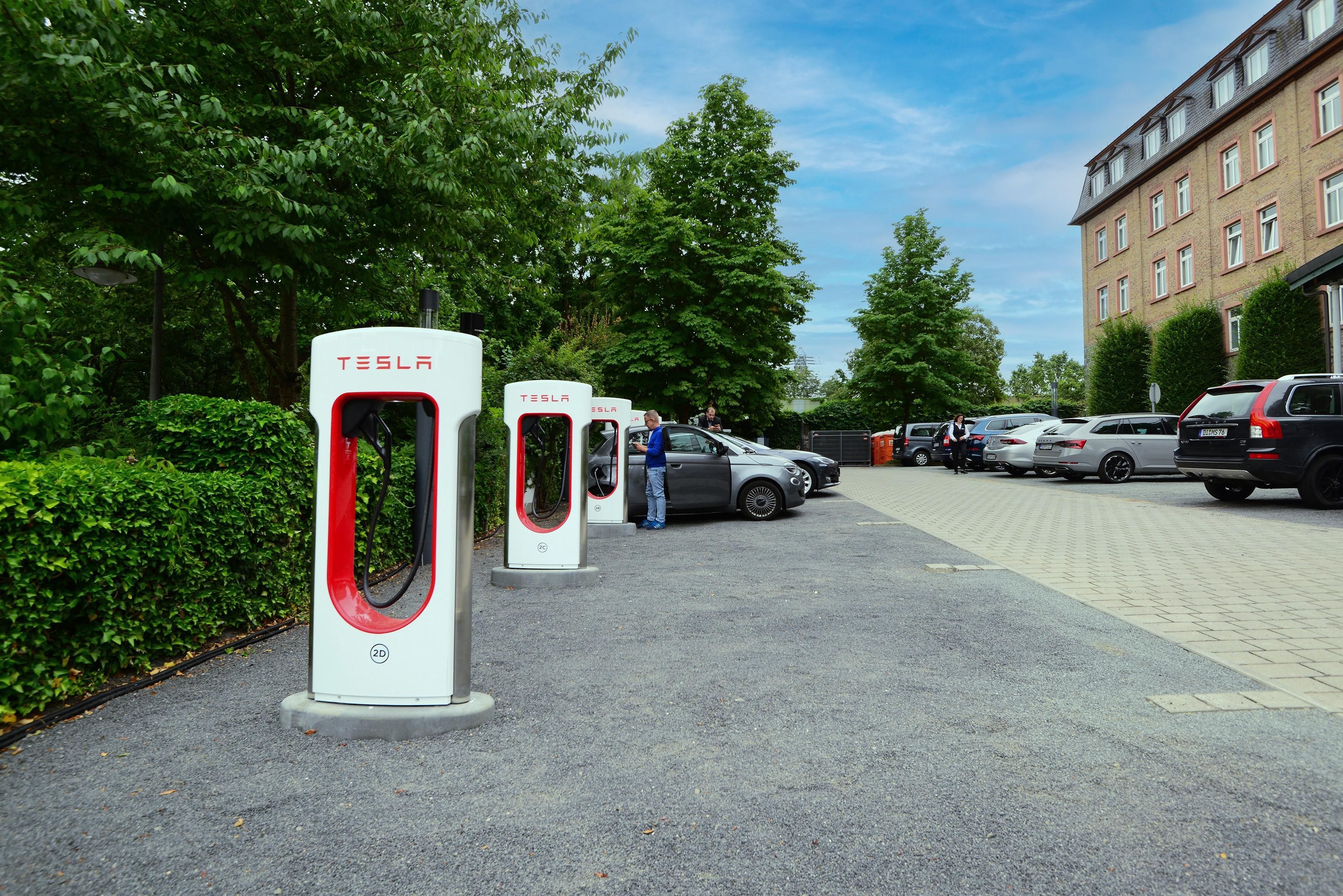 A parking area with electric vehicle charging stations, a building with multiple windows, and a clear sky.