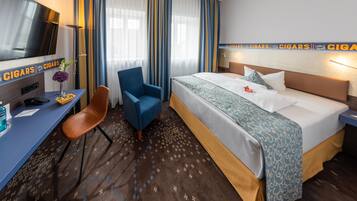 A hotel room with a bed, a desk, a chair, a TV, and a wall with cigar-themed decorations.