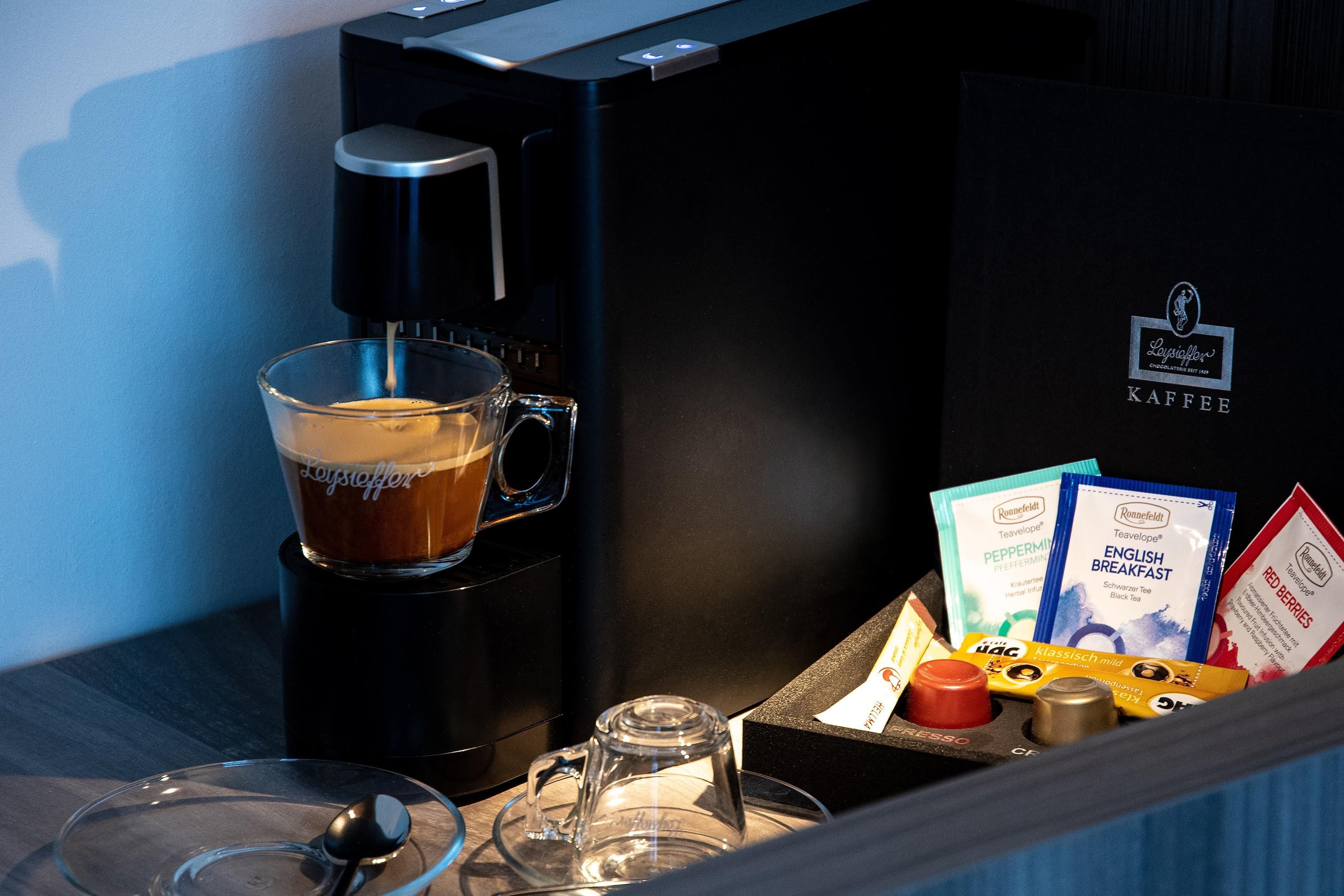 Una cafetera con una taza de café, una jarra de vidrio y cápsulas de café.
