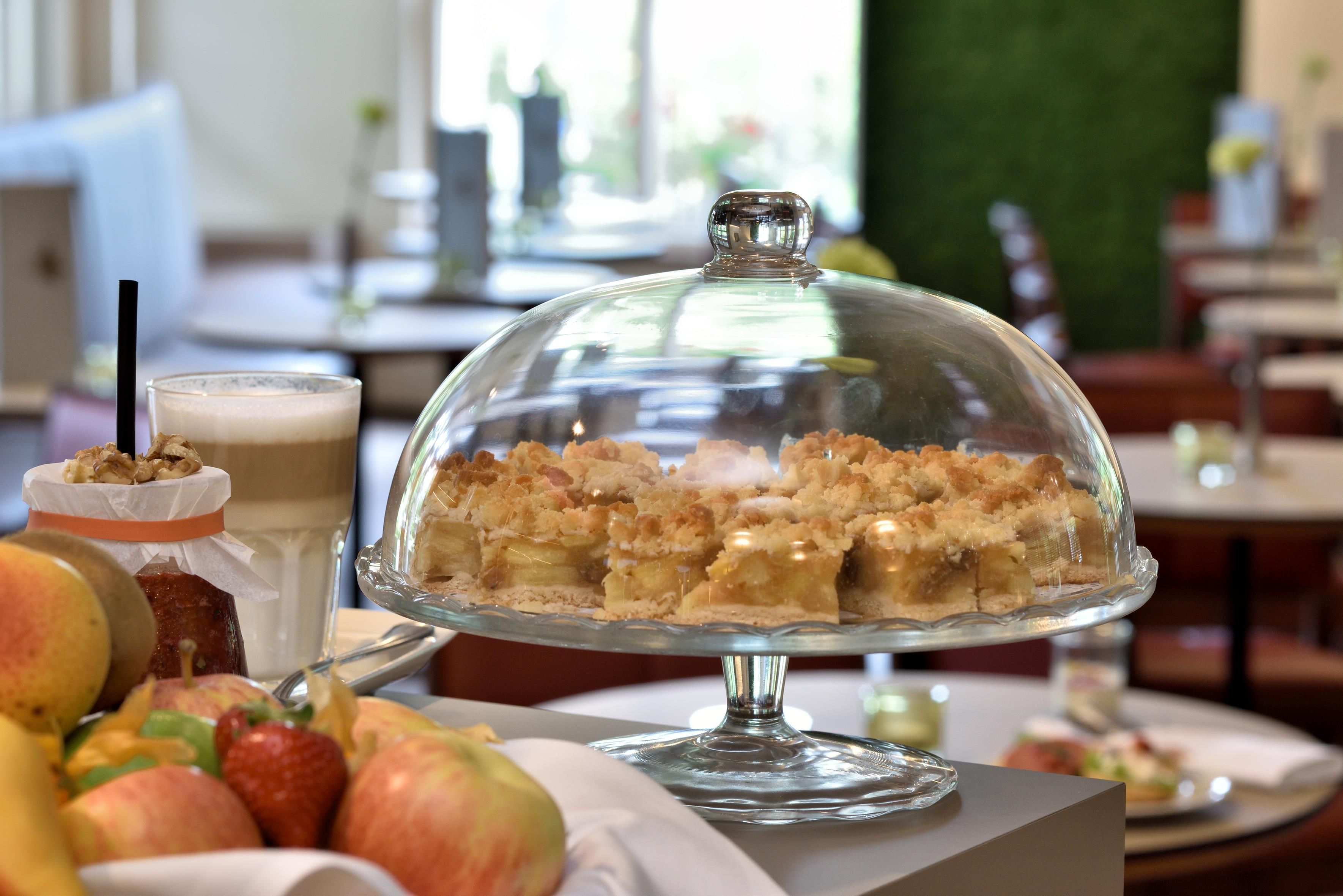 A dessert display with a glass dome cover, a beverage with a straw, and a plate of fruit.