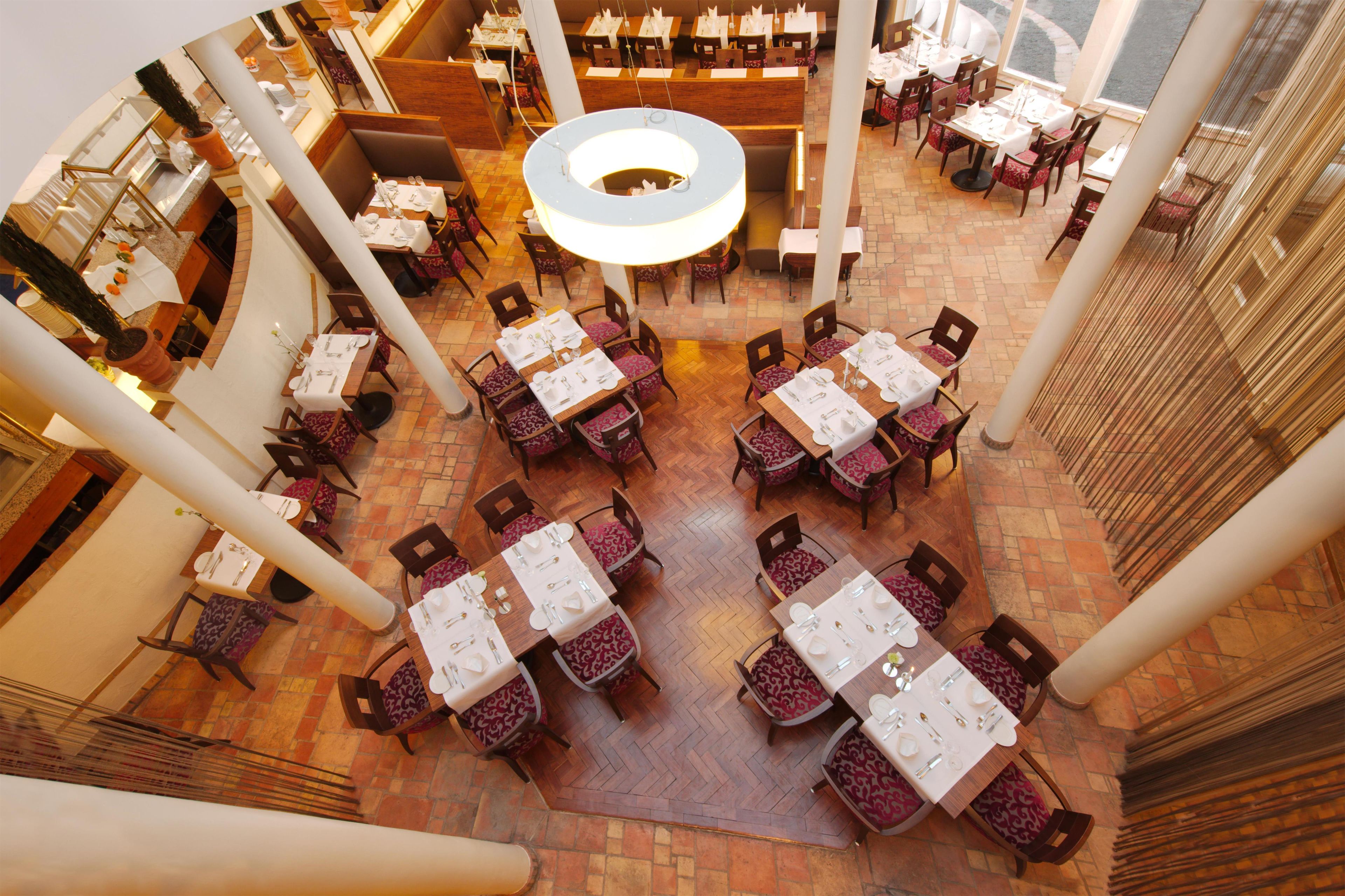 Un comedor interior con varias mesas y sillas, un candelabro circular en el centro, y suelo de baldosas.