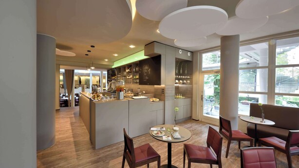 Un restaurante moderno con barra central, zona de estar y amplios ventanales que ofrecen vistas de la calle.