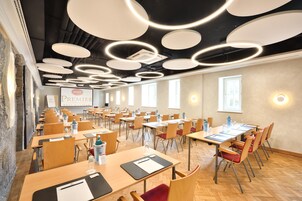 Un salón de conferencias con varias mesas y sillas, una pantalla de proyector y un letrero que indica 'Premier Best Western'.