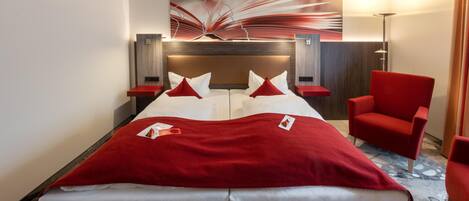 Une chambre d’hôtel avec un lit, des chaises rouges, une couverture rouge et une œuvre d’art murale.