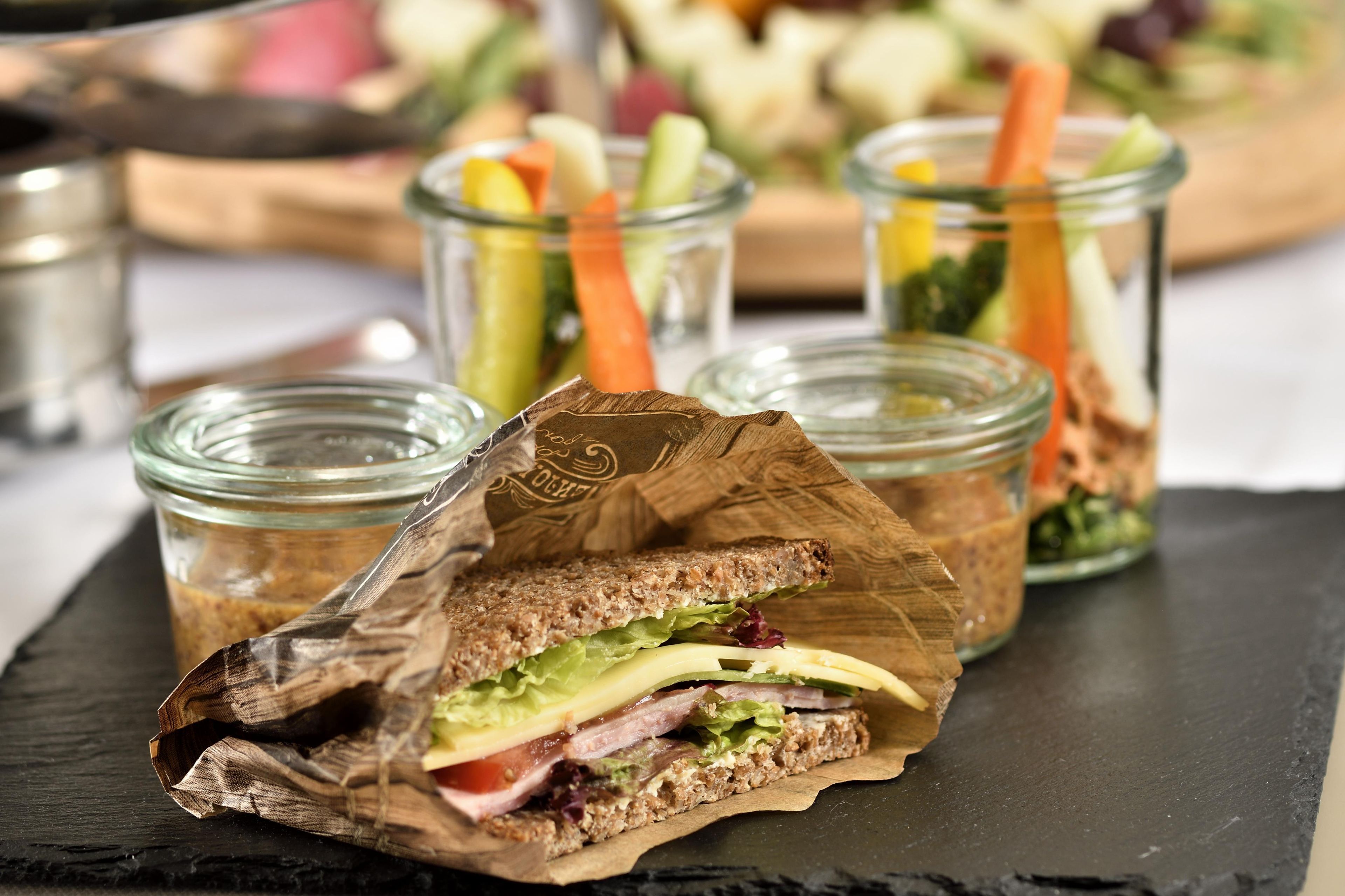 A sandwich on a slate board, with a salad and drinks in the background.