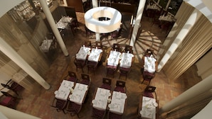 A restaurant with multiple tables set for dining, large columns, and a central chandelier.