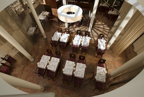 Un restaurant doté de nombreuses tables dressées pour le service, de grandes colonnes et d’un lustre central.
