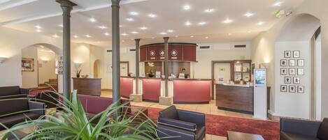A hotel lobby with a reception desk, seating area, and a staircase.