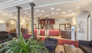 Un vestíbulo de hotel con una recepción, zona de estar y una escalera.