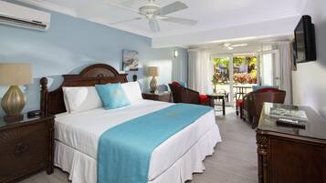 A hotel room with a large bed, a ceiling fan, a TV, and a view of the outside balcony.