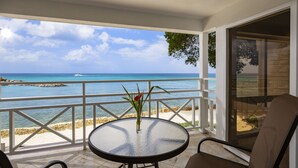 A balcony with a glass table and chairs, overlooking a beach and the sea.