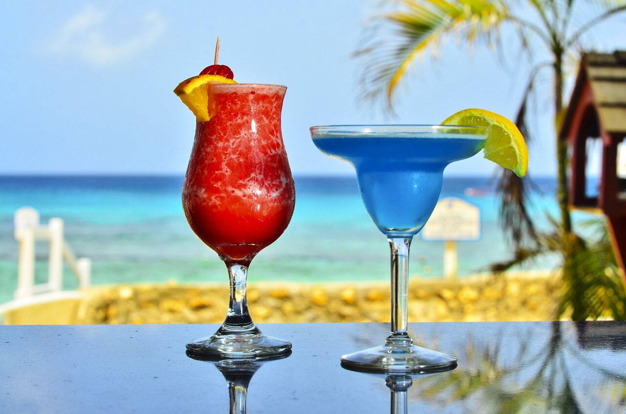 Two cocktails on a table with a beach and ocean view in the background.