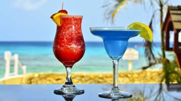 Two cocktails on a table with a beach and ocean view in the background.
