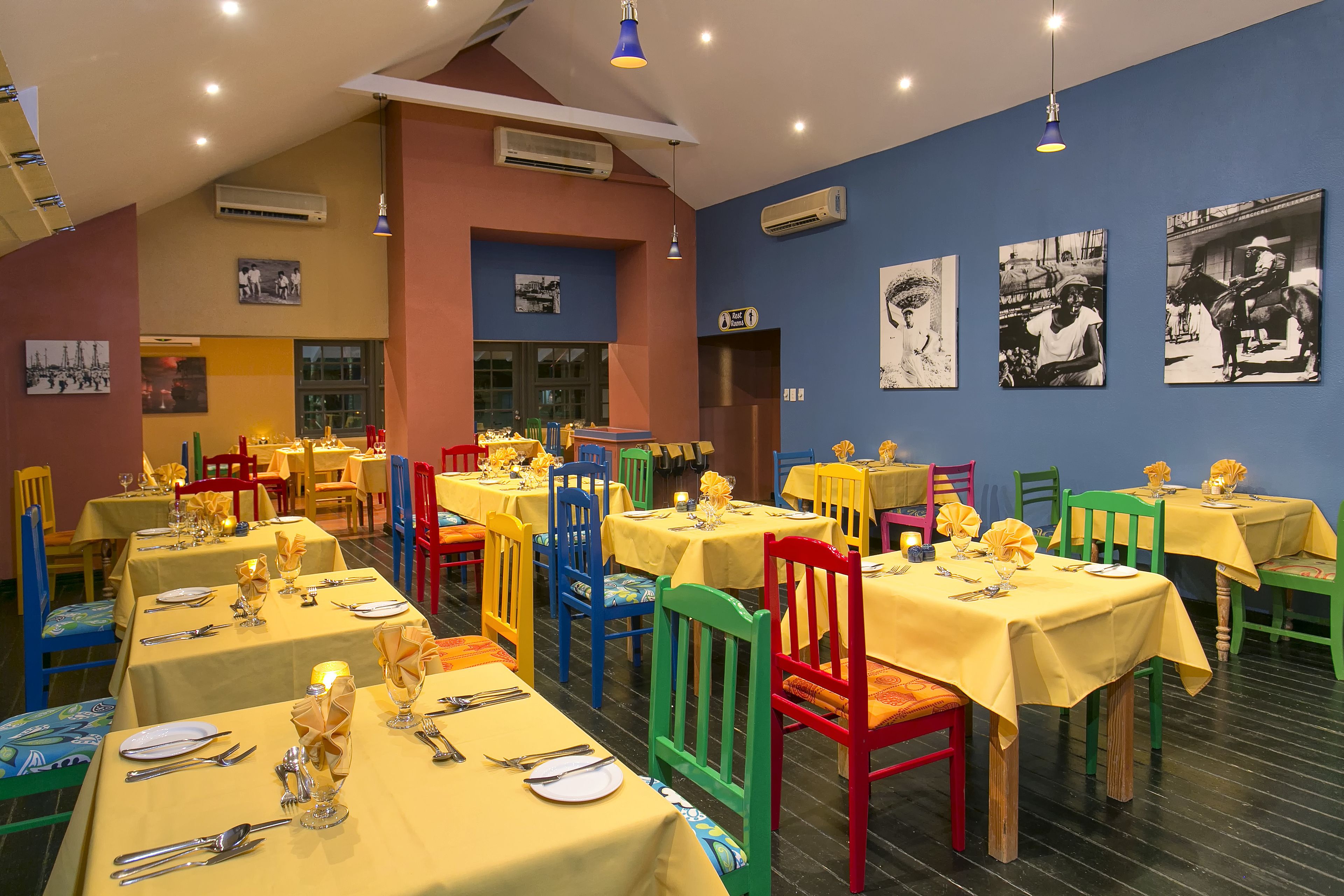 Un comedor con varias mesas, sillas coloridas y obras de arte blanco y negro en las paredes.