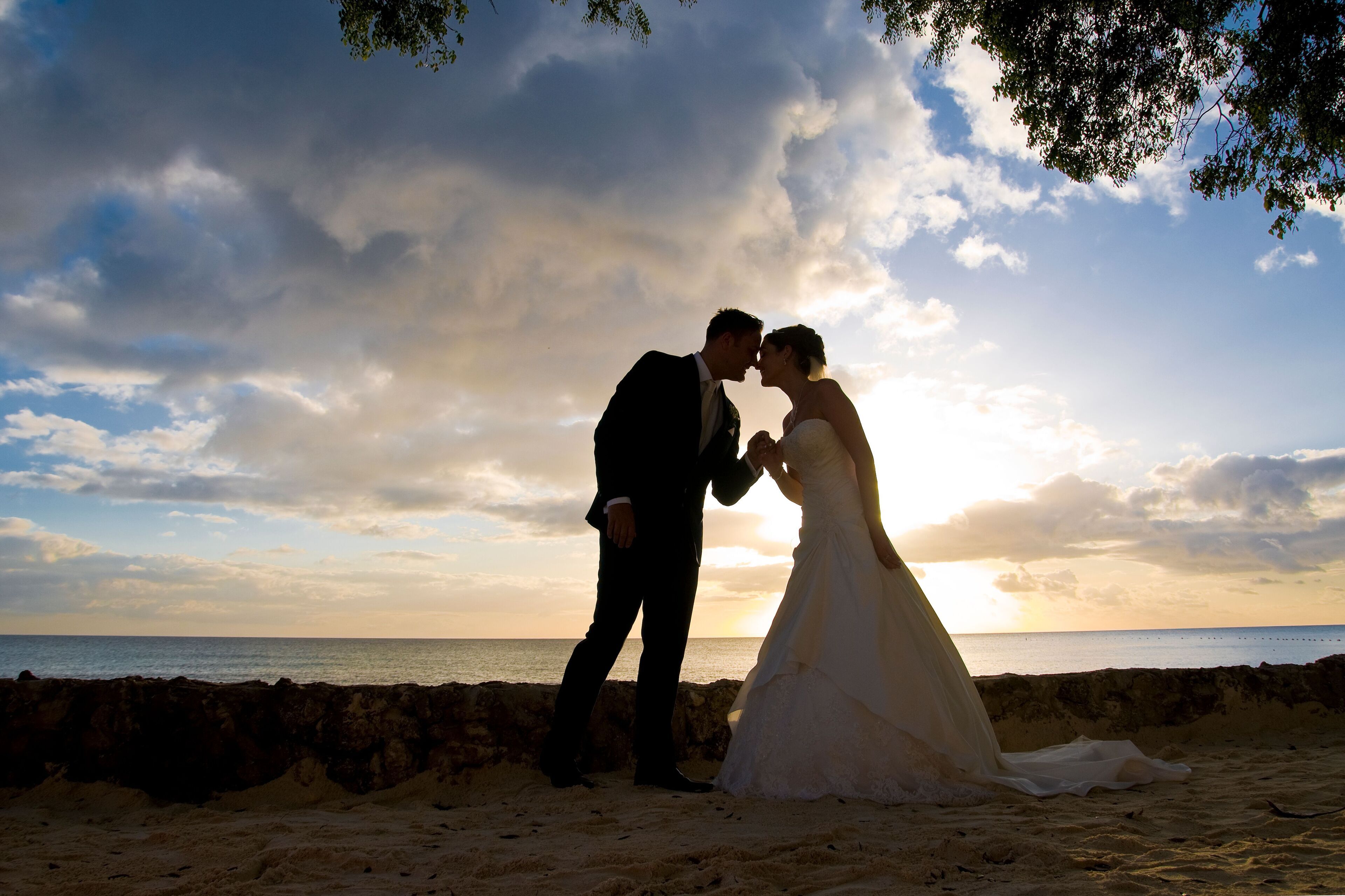A couple embracing on a beach with a sunset in the background.