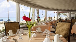 A dining area with tables set for service, chairs, and a view of the beach.