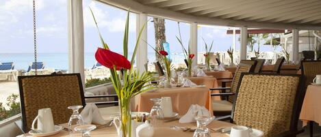 Un espace repas avec des tables dressées, des chaises et une vue sur la plage.