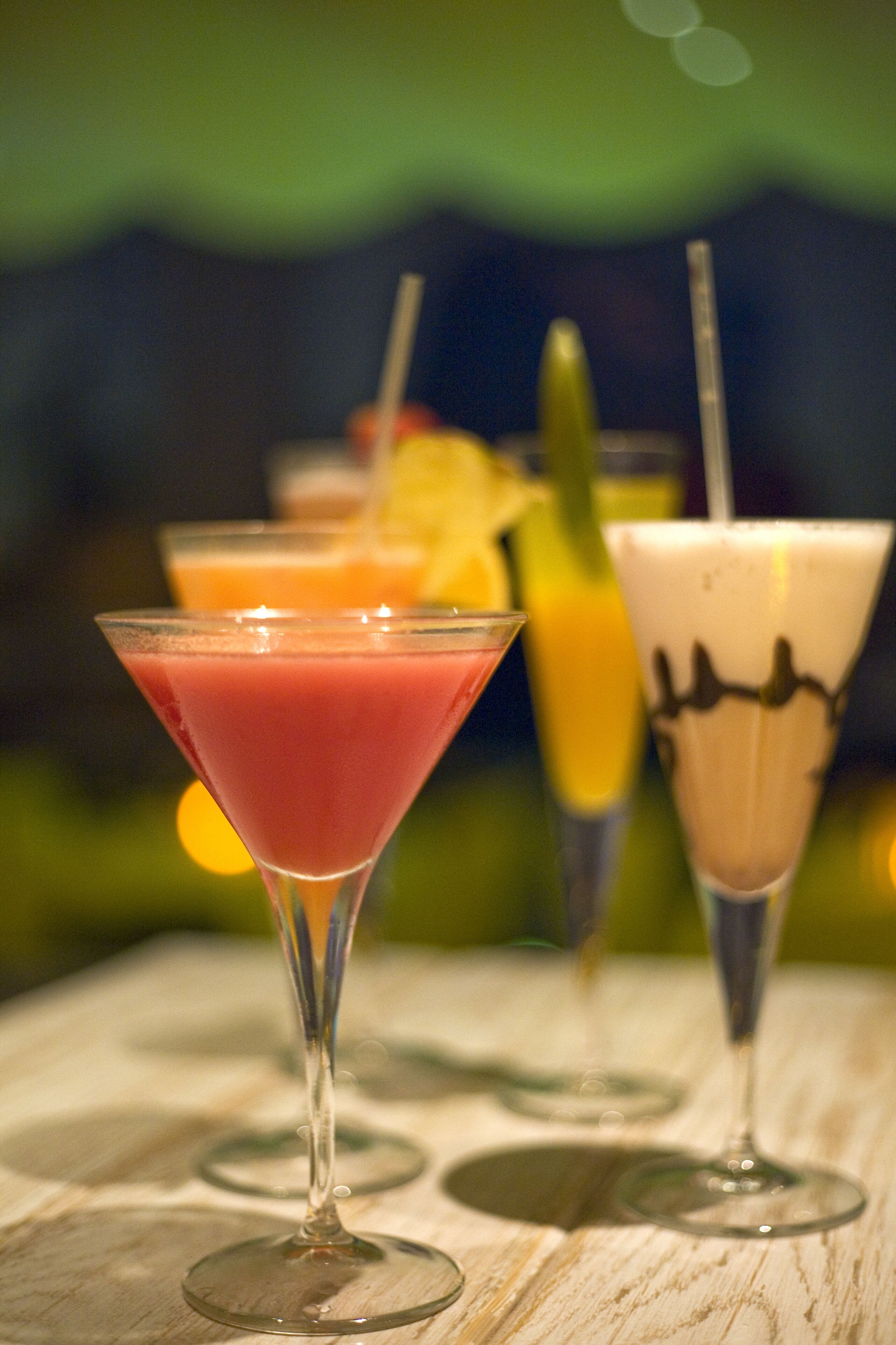Three drinks in martini glasses on a wooden table with a blurred background.